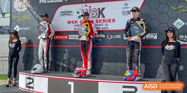 A student from Suzhou North America High School is standing on a podium with a trophy and a race suit.