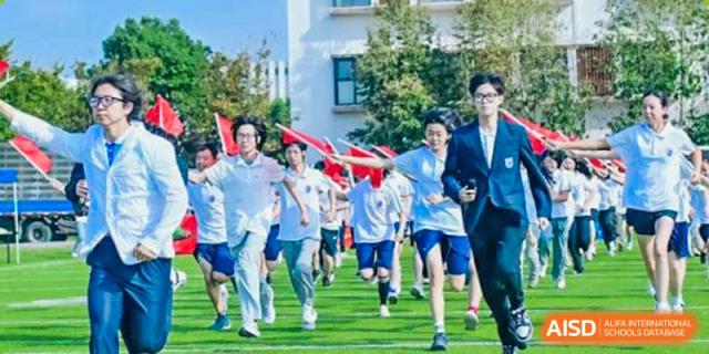 Students from Suzhou North America High School are running on a field with flags during a sports day.