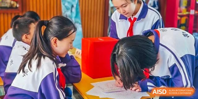 Two students from Tianjin Nankai High School are working together on a project that involves a red box on a desk.