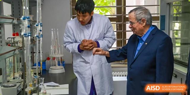 Two male students from Tianjin Nankai High School  are wearing lab coats and conducting a science experiment with a teacher.