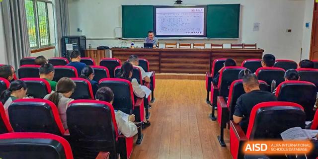 Students from Tianjin Nankai High School  are seated in a long row of red chairs, facing forward.