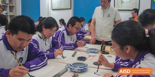 Two male students from Tianjin Nankai High School  are engaged in a traditional calligraphy activity at a table.