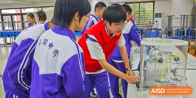 Two male students from Tianjin Nankai High School  are working on a project together, with one student wearing a red vest over his uniform.