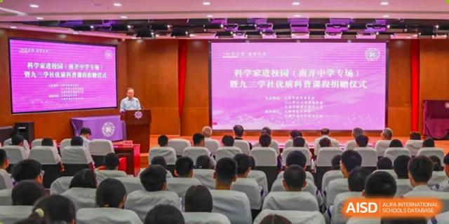 A view from the back of an audience of students from Tianjin Nankai High School , watching a presentation on a large screen in an auditorium.