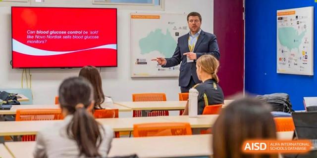 A male teacher from Wellington College International Tianjin points at a screen while teaching students in a classroom.