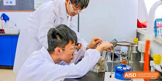 Two male students from Wellington College International Tianjin in lab coats work on a science project together.