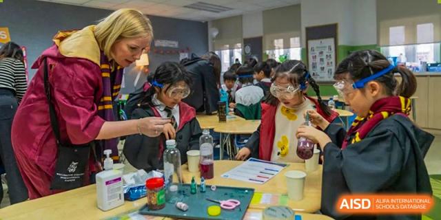 Wellington College International Tianjin students in lab coats and safety goggles conduct a colorful experiment at a table.
