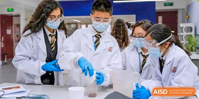 A male student from Wellington College International Tianjin in a lab coat and safety goggles pours a liquid from a beaker.