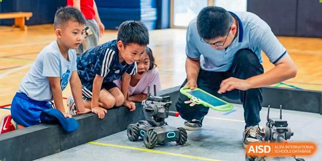 A male teacher from Wellington College International Tianjin helps two students with a remote-controlled robot.