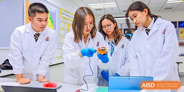 Two female students from Wellington College International Tianjin in lab coats work on a device with wires.