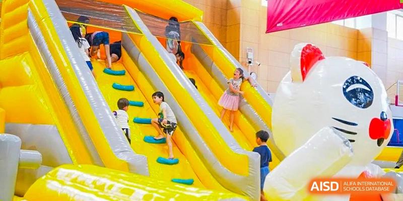 Students from Wellington College International Tianjin play on a large yellow inflatable slide outdoors.