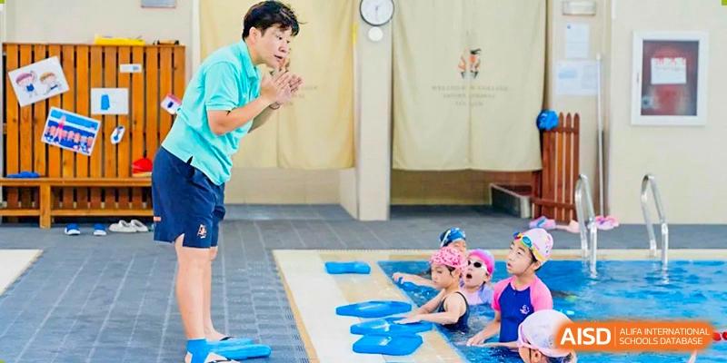 A swim instructor from Wellington College International Tianjin teaches two young children in a swimming pool.