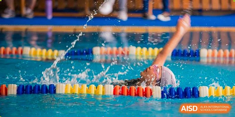 A student from Wellington College International Tianjin swims in a pool, creating a splash, with lane dividers visible.
