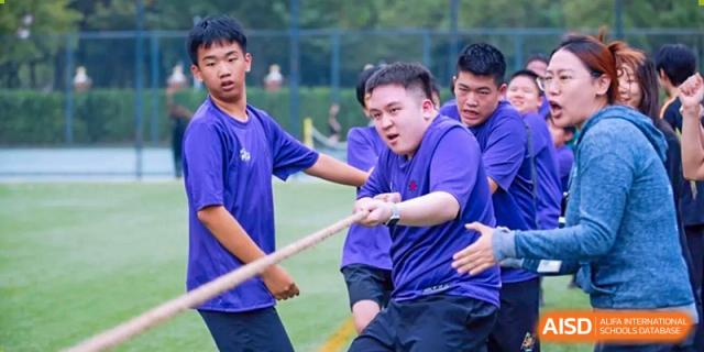 A group of male students from Wellington College International Tianjin participates in a tug-of-war competition outdoors.