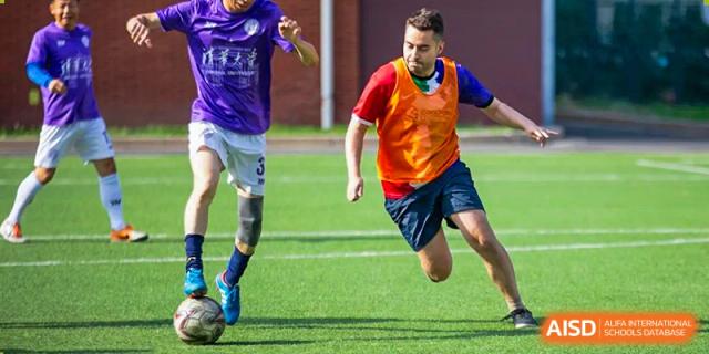 Students from Wellington College International Tianjin play soccer on a field, with one student in a red shirt running with the ball.