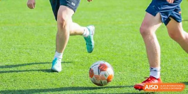 A close-up of a Wellington College International Tianjin student's foot next to a soccer ball on a green field.