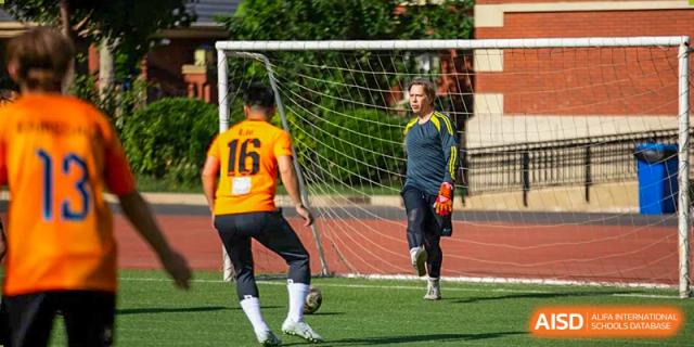 A Wellington College International Tianjin student in an orange jersey practices soccer drills while a teammate watches.