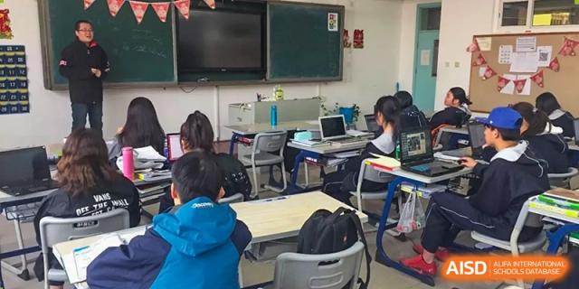 Students working on laptops or notebooks at their desks in a classroom setting at Yang Guang Qing International School of Beijing.