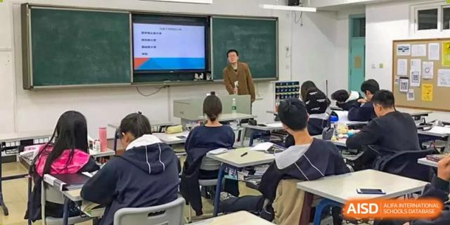 A teacher standing in front of a smart board leading a class discussion with seated students at Yang Guang Qing International School of Beijing.