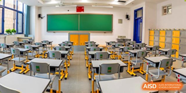 An empty, brightly lit classroom featuring rows of desks and a large green chalkboard at Yang Guang Qing International School of Beijing.