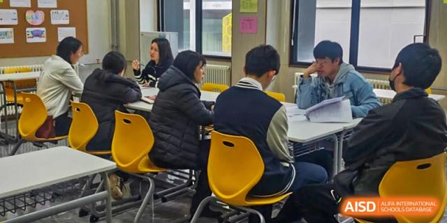 A small group of students and an instructor engaged in a discussion or working together around a table at Yang Guang Qing International School of Beijing.