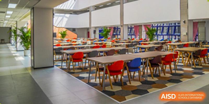 The spacious, modern cafeteria or dining hall with multiple tables and colorful chairs at Yang Guang Qing International School of Beijing.