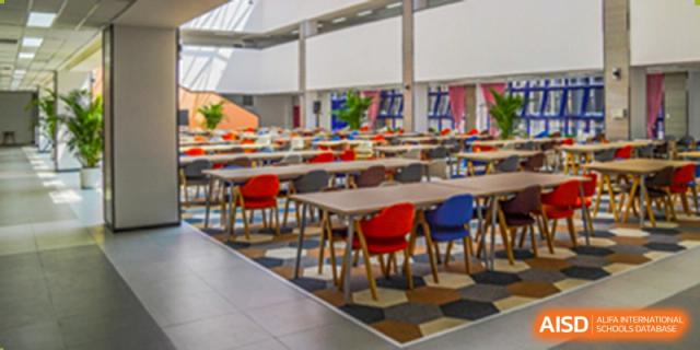 The spacious, modern cafeteria or dining hall with multiple tables and colorful chairs at Yang Guang Qing International School of Beijing.