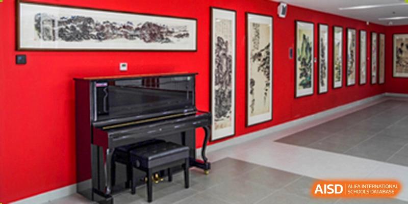 A black grand piano set against a red wall with framed traditional artwork at Yang Guang Qing International School of Beijing.