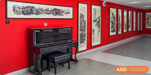A black grand piano set against a red wall with framed traditional artwork at Yang Guang Qing International School of Beijing.
