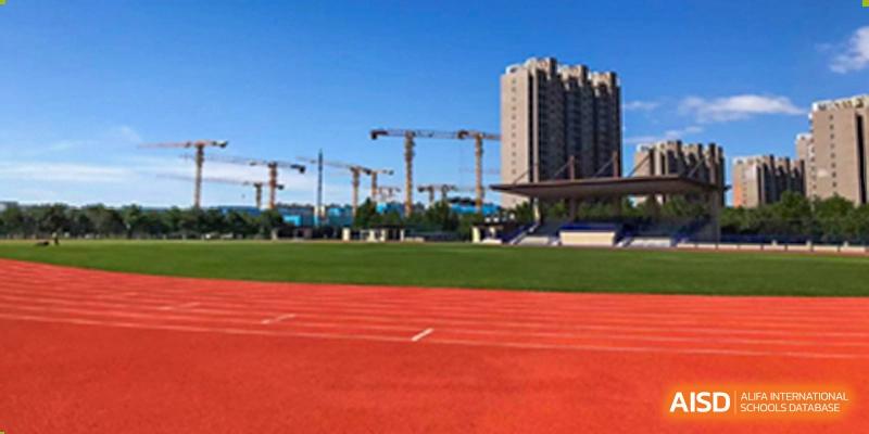 A close-up of a red running track surface with a view of buildings and construction cranes in the background at Yang Guang Qing International School of Beijing.