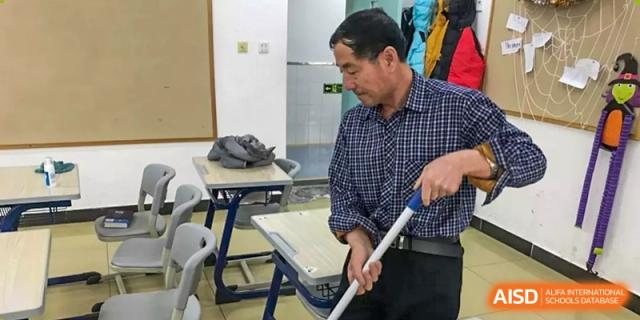 A staff member mopping or cleaning the floor of a classroom or dormitory at Yang Guang Qing International School of Beijing.