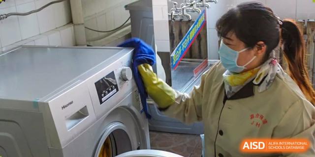 A staff member wearing yellow gloves cleaning the exterior of a washing machine or dryer at Yang Guang Qing International School of Beijing.