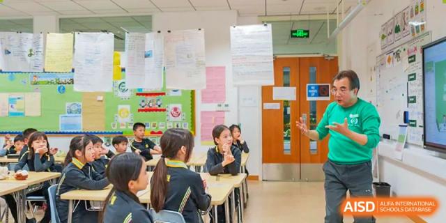 A teacher interacting with Huili School Shanghai students seated at a classroom desk during a focused discussion.