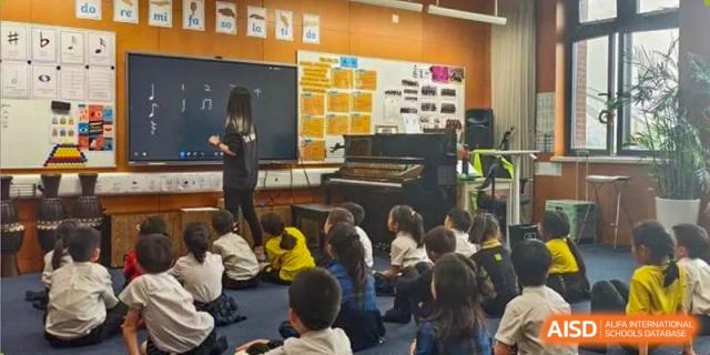 Huili School Shanghai students gathered on the floor watching a presentation near a blackboard and piano.
