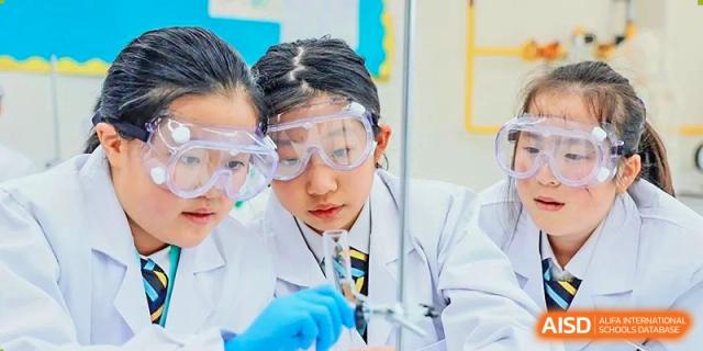 Huili School Shanghai students wearing lab coats and safety goggles performing an experiment in a science laboratory.