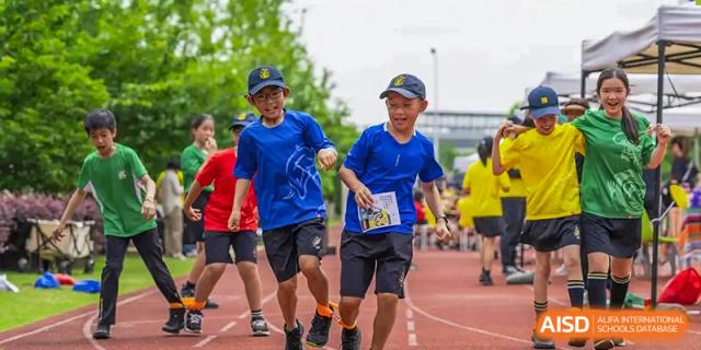 Two smiling Huili School Shanghai students running and competing on an outdoor track during a sports day or field event.