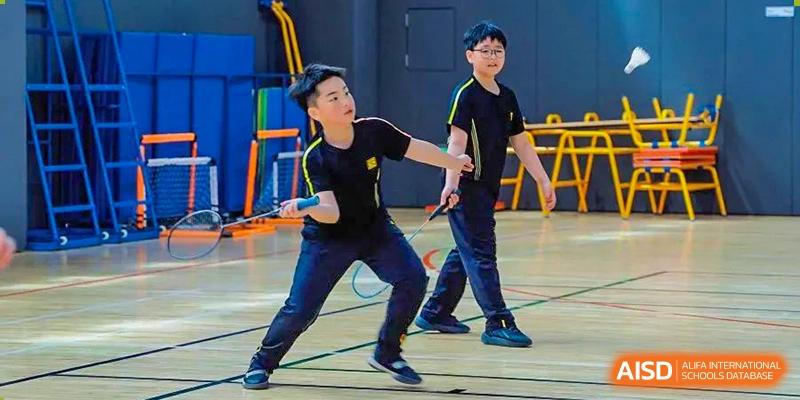 A Huili School Shanghai student actively playing badminton with a racket in an indoor gymnasium setting.