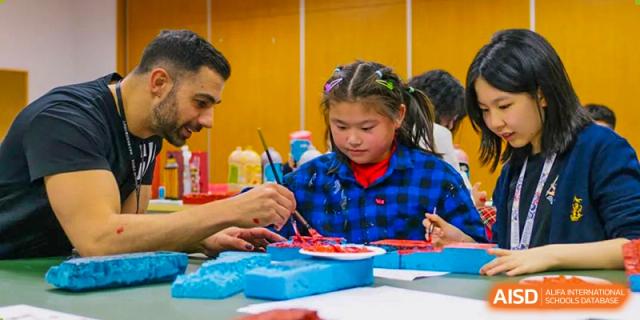 A young Huili School Shanghai student doing hands-on art and crafts with a teacher's guidance.
