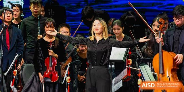 A music teacher conducting the Huili School Shanghai student orchestra or string ensemble during a performance.