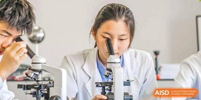 A female student in a lab coat looking into a microscope at Yew Wah International Education School of Shanghai Gubei.