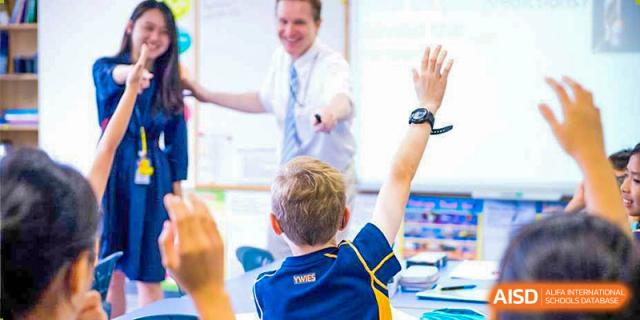 A teacher engaging with a young student who has his hand raised in a classroom at Yew Wah International Education School of Shanghai Gubei.