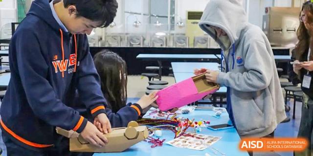 A student holding a pink object and working with electronics and wires at Yew Wah International Education School of Shanghai Gubei.
