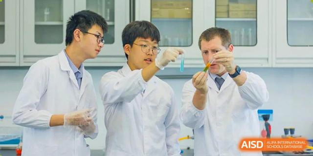 A male student in a lab coat looking at a test tube while a teacher watches at Yew Wah International Education School of Shanghai Gubei.