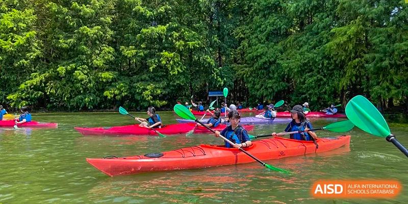 Students in kayaks on a lake, paddling near a tree-lined shore at Yew Wah International Education School of Shanghai Gubei.