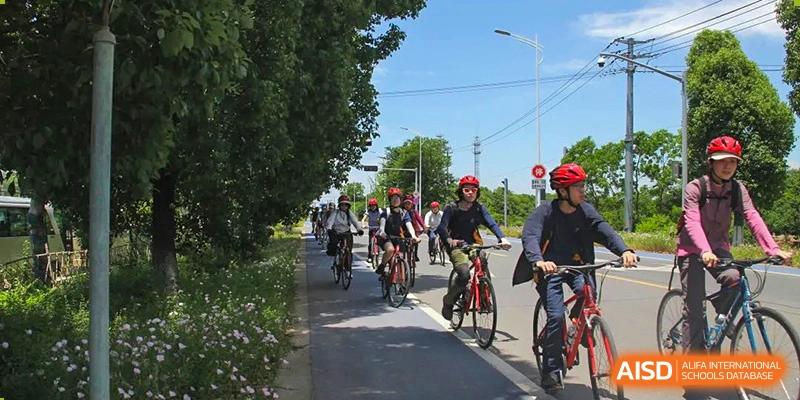 A group of students riding bicycles on a paved path at Yew Wah International Education School of Shanghai Gubei.