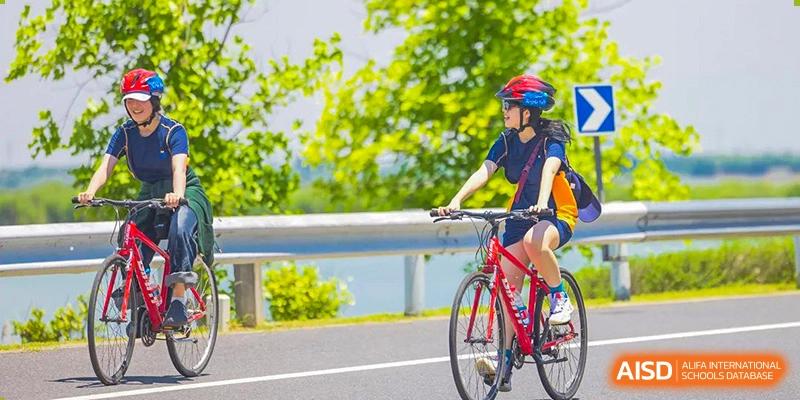 A female student wearing a helmet and riding a bicycle on a road at Yew Wah International Education School of Shanghai Gubei.