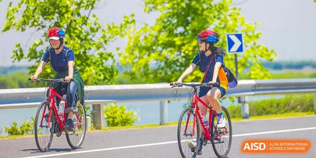 A female student wearing a helmet and riding a bicycle on a road at Yew Wah International Education School of Shanghai Gubei.