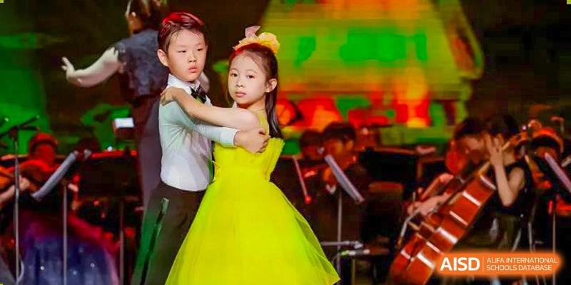 A young girl in a yellow dress dancing with a boy on a stage during a school performance at Yew Wah International Education School of Shanghai Gubei.