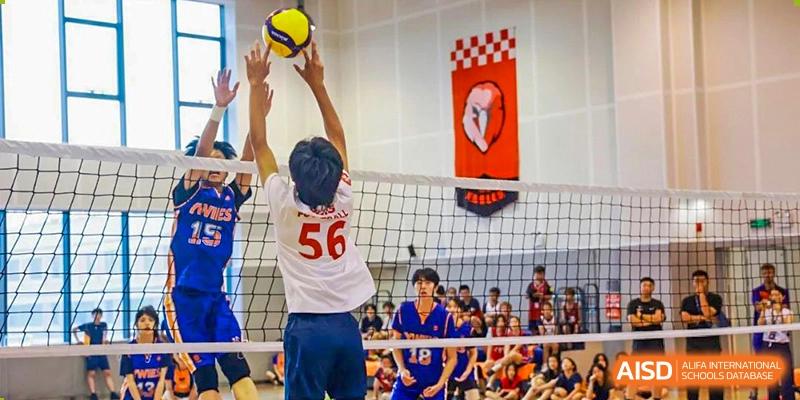 A male student reaching over the net to hit a volleyball during a game at Yew Wah International Education School of Shanghai Gubei.