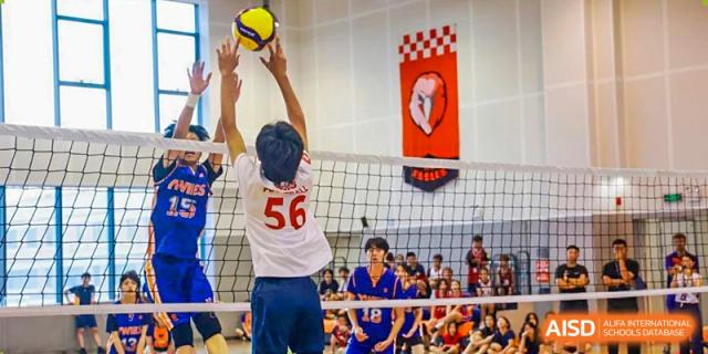 A male student reaching over the net to hit a volleyball during a game at Yew Wah International Education School of Shanghai Gubei.